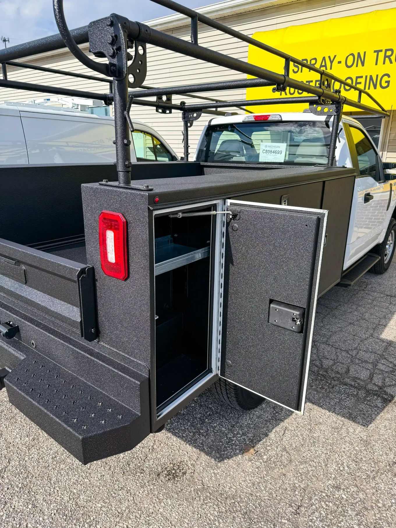Commercial service body truck fully coated in textured black protective coating, with toolbox compartment open