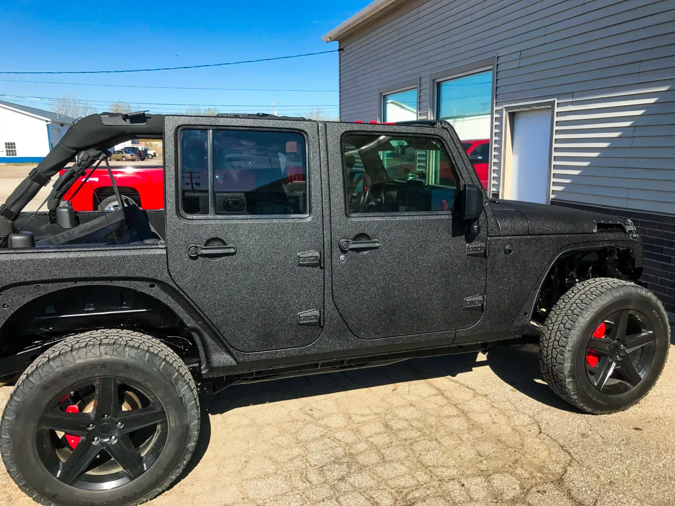 Jeep Wrangler Unlimited with full-body spray-on textured black coating and red wheel accents
