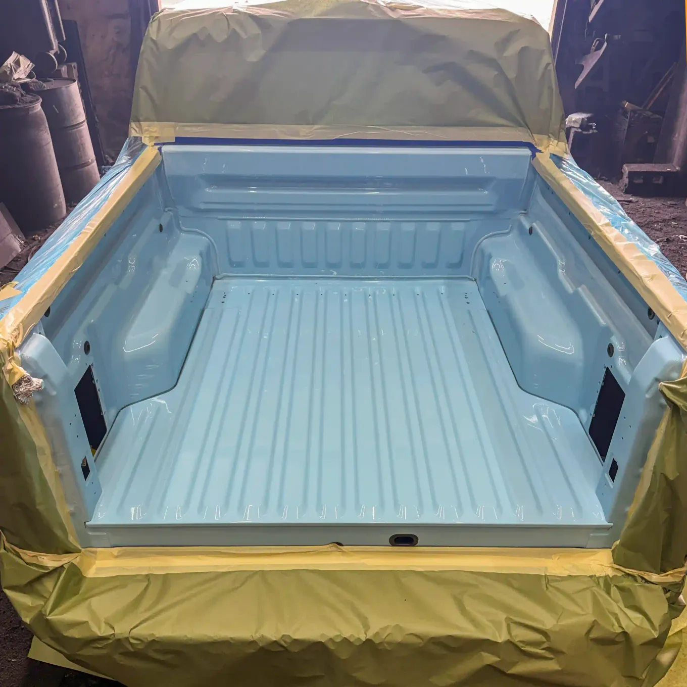 Truck bed sprayed in a custom color-matched light blue bedliner, masked off in the spray booth